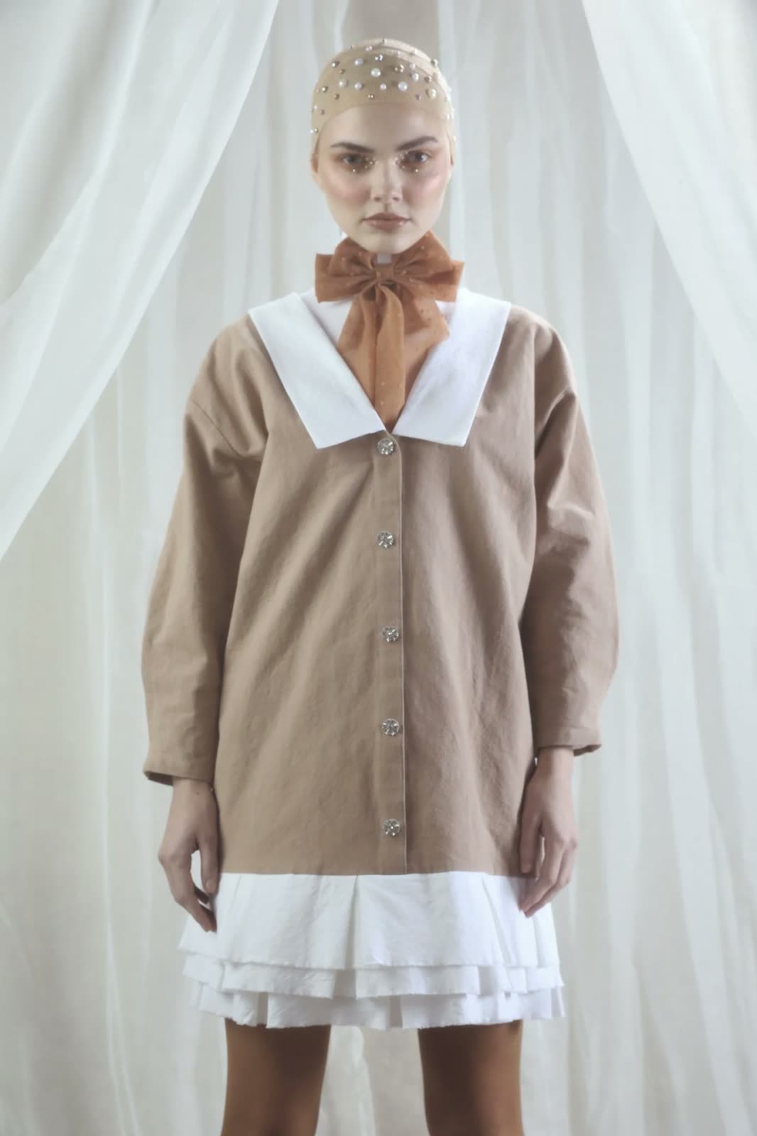 Woman in a pearl-studded skullcap and tan dress with a white sailor collar and rust organza bow