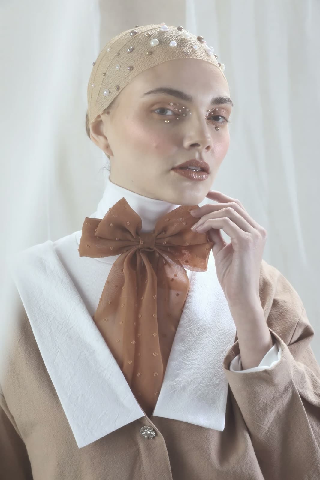 Close-up of a woman in a pearl skullcap, gems on her face, holding a rust organza bow