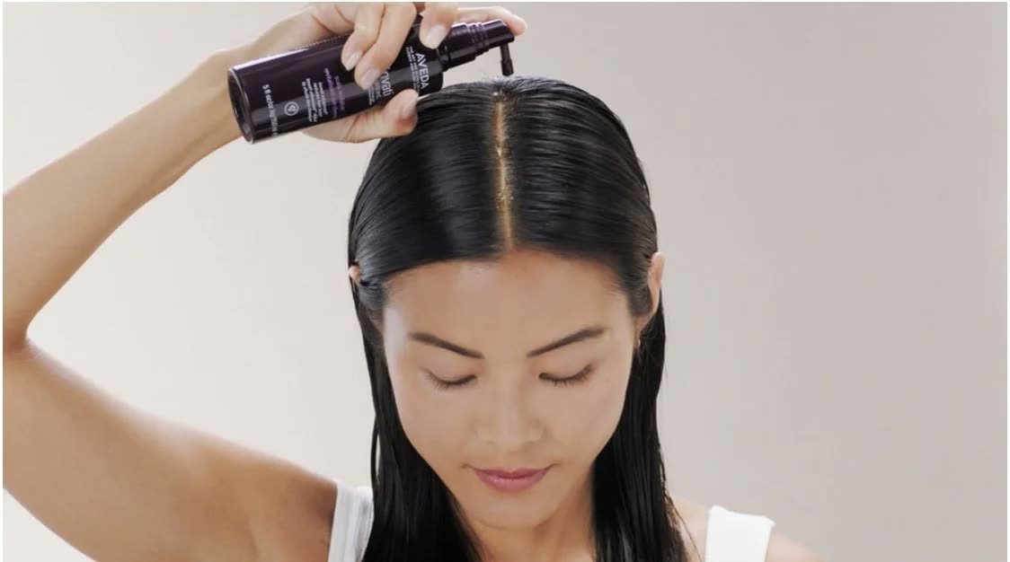 Woman with sleek black hair applies serum to her scalp from a dropper bottle