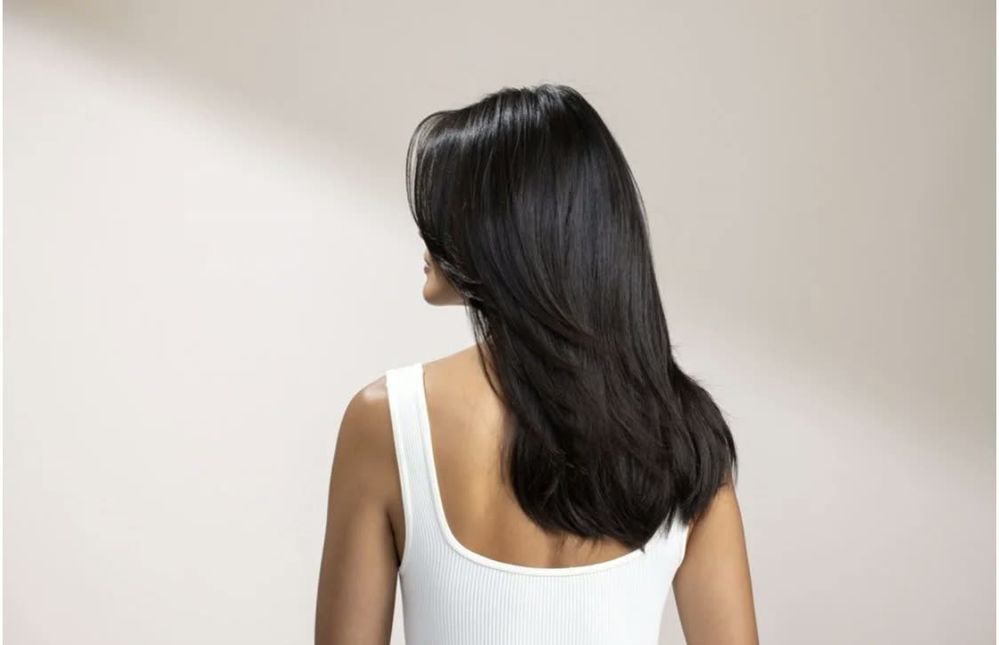 Back view of a woman with long layered black hair in a white tank top