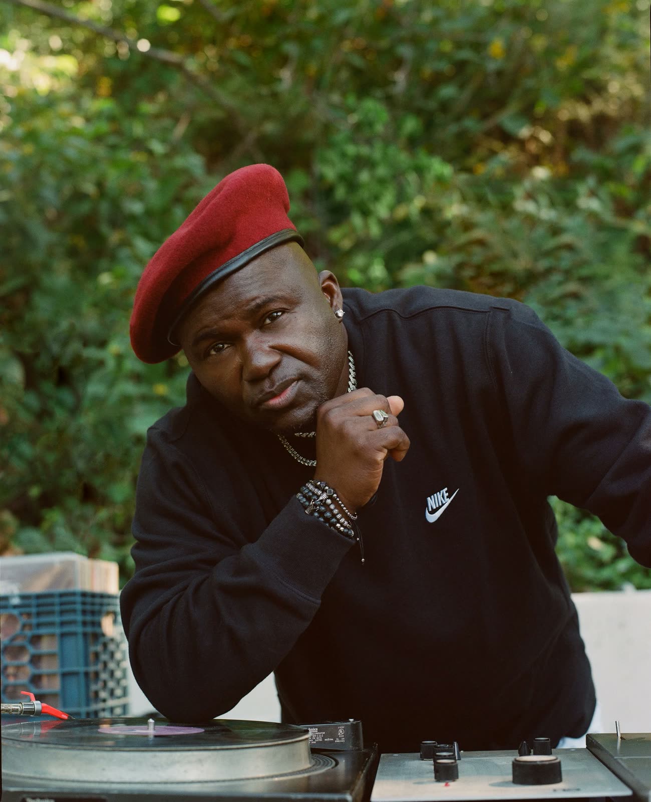 DJ in a red beret and black Nike sweatshirt leans over a turntable