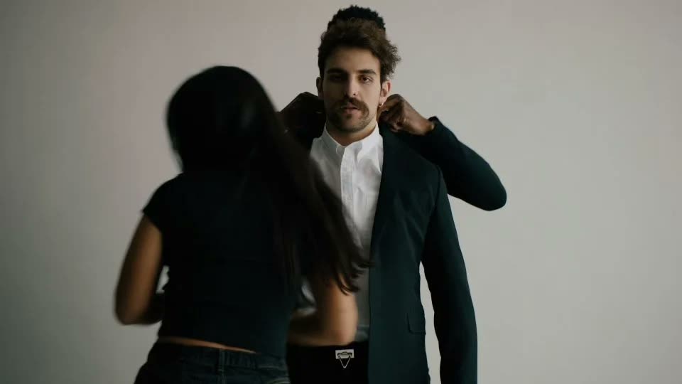 Woman adjusts the collar of a man's black suit jacket over a white shirt, Facetime video still