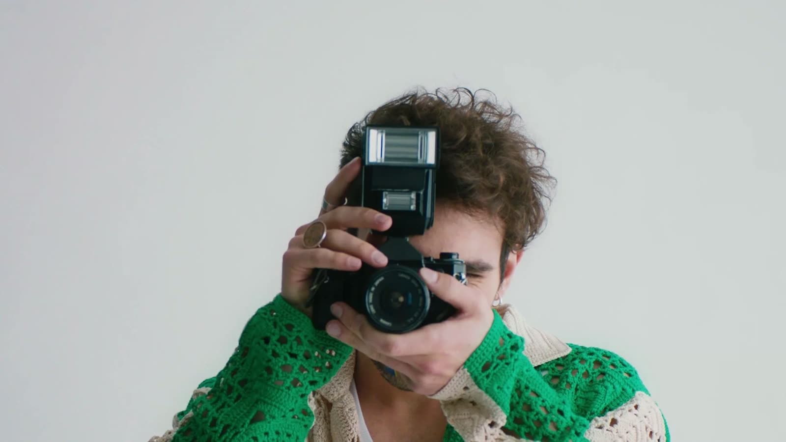 Man in a green crochet cardigan holds a camera up to his face, Facetime video still