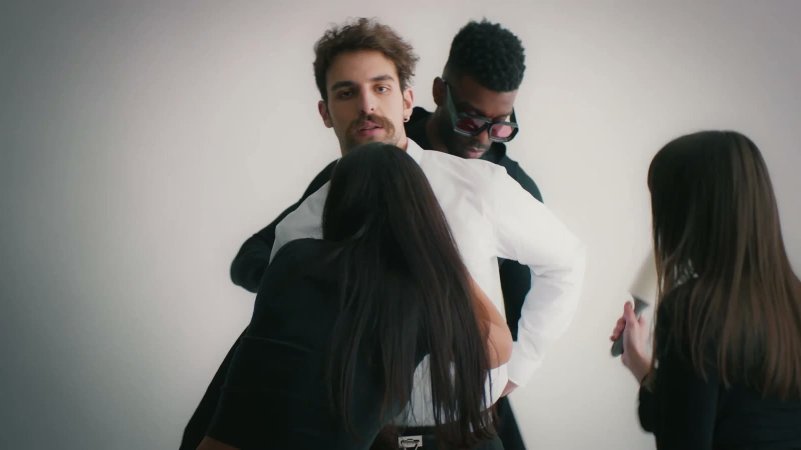 Crew dress a man in a white shirt and black blazer on a white set, Facetime video still